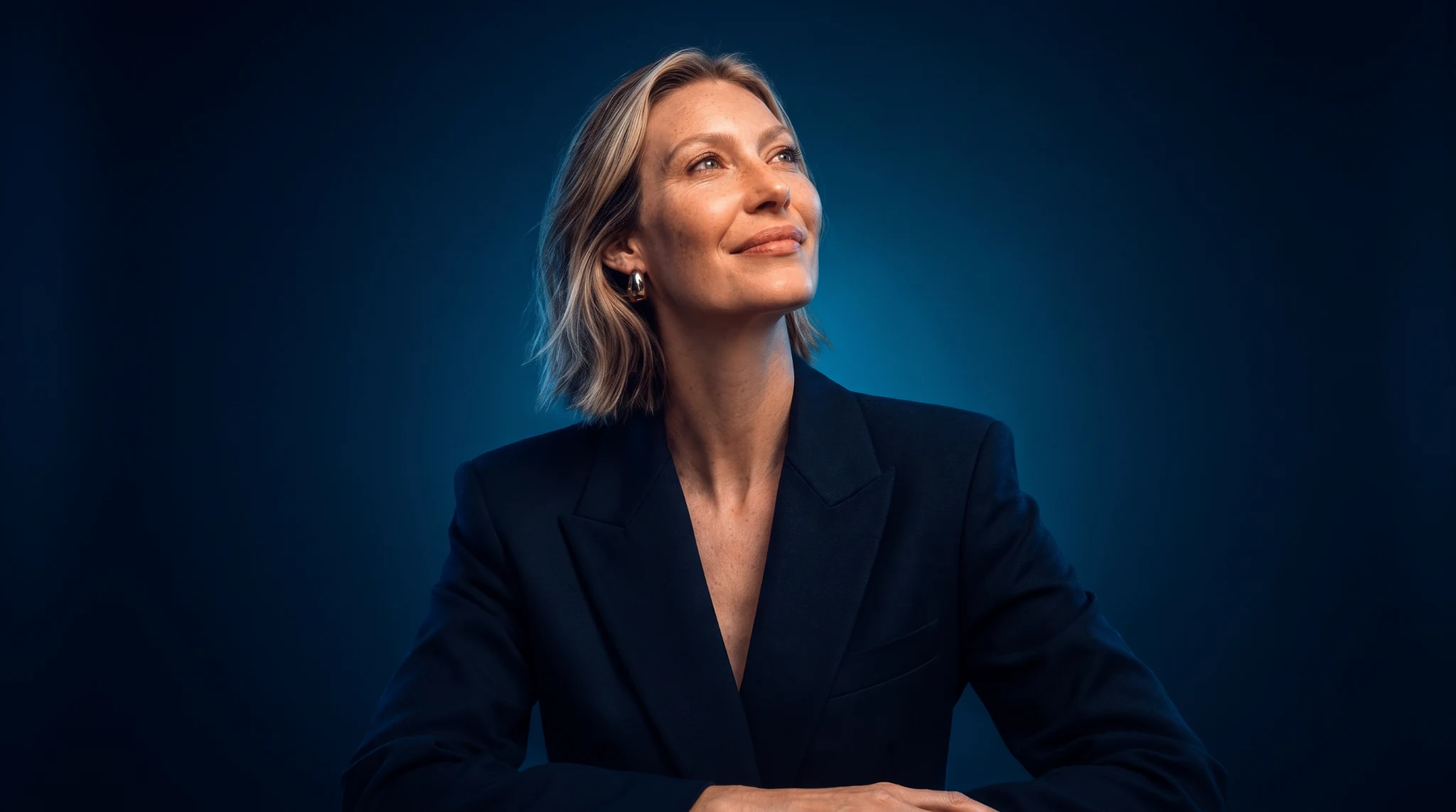 A woman in a navy blazer looking upwards against a blue background
